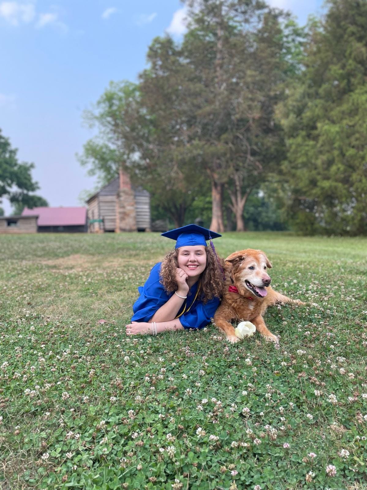 Nia in cap and gown lying in the grass beside a senior golden retriever
